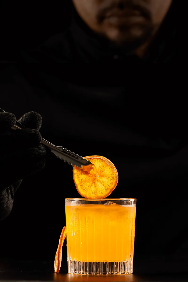 Bartender garnishing an orange cocktail with a dried orange slice